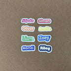 A grid of eight 2-inch wide custom name stickers showcasing all available colors, including red (Simon), orange (Oliver), and purple (Mandi).
