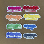 A grid display of eight custom name stickers featuring a polyhedral dice design in various colors including pink, red, orange, yellow, green, blue, dark blue, and grey.